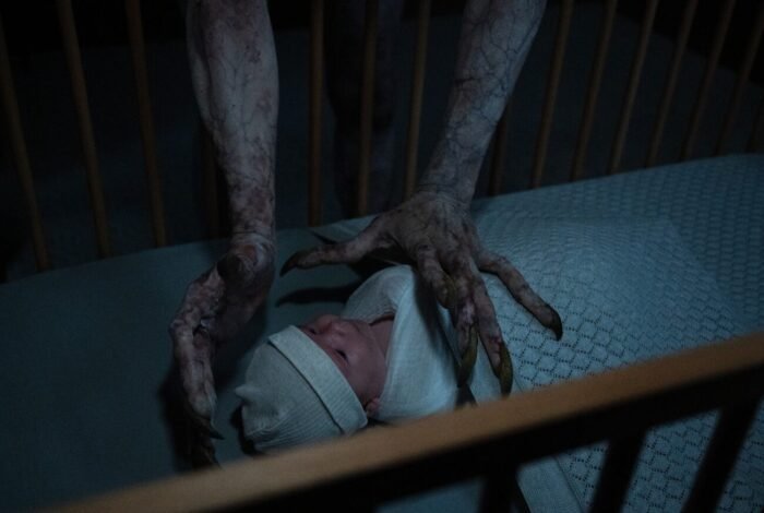 two dirty and decrepit hands reach into a baby's crib in THE MOOGAI