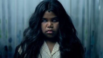 A child with dark, flowing hair is seen expressionless with white eyes.