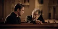 A young priest speaks to an old man in the pews of a church in THE RITUAL.