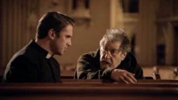 A young priest speaks to an old man in the pews of a church in THE RITUAL.