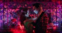 A man and woman embrace in front of a fish tank under neon red and pink lights.