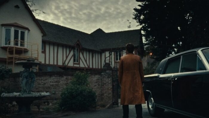 A woman standing beside a classic car, looks at the large house on the property
