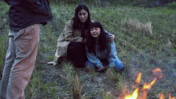 A woman consoles a younger woman in a field inches from a fire
