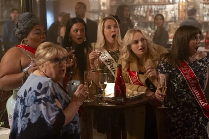 A group of women sit at a table with surprised expressions in BRIDE HARD