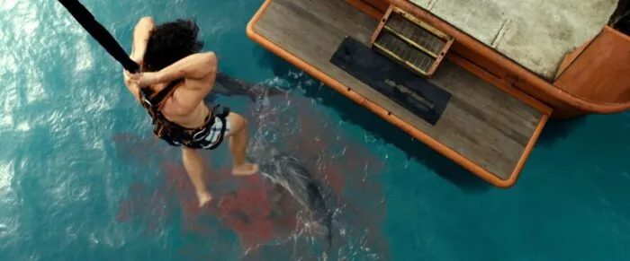 A woman is strung up to a crane over circling sharks in the ocean below in DANGEROUS ANIMALS.