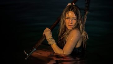 Zephyr is in the water with a spear, preparing for a shark attack