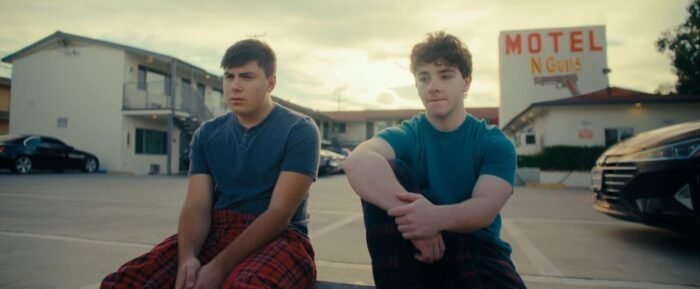 Two teenagers sit at the edge of a motel parking lot.