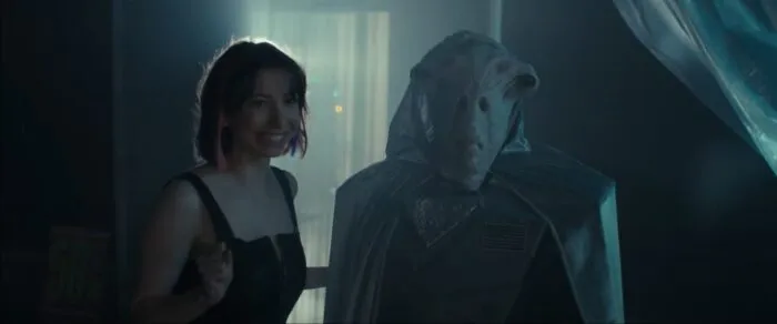 A woman stands beside an alien in a doorway