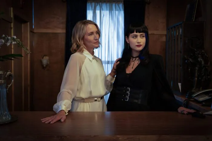 Two women stand in front of a window, behind a desk