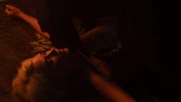 A cloaked figure is holding a knife to the neck of a woman lying on the floor (Hell Motel)