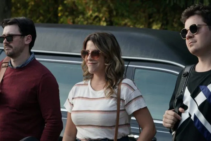 two men and a woman are wearing sunglasses outside of a limousine.