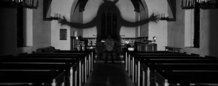 an ominous shadow fills the space between the pews of a church in OBEX