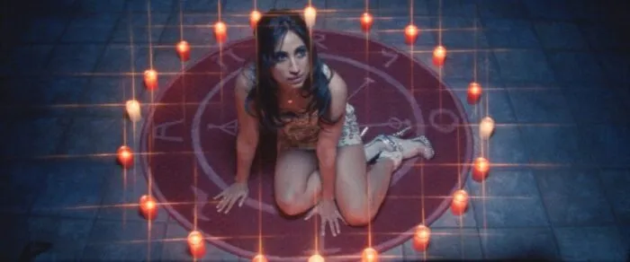 A woman sits in a red circle surrounded by candles