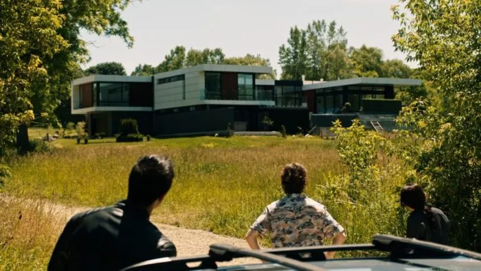 Two people view a large house from outside of a car.