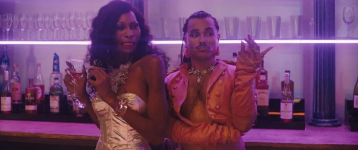 Two drag queens are seen standing at a nightclub bar, one looks disgusted.