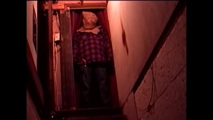 A man with a potato sack on his head stands in the doorway at the top of a staircase