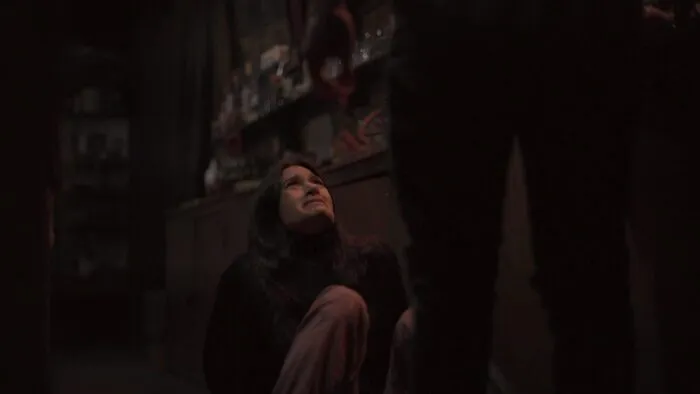 A young woman looks scared as she looks up at the shadowy figure standing over her