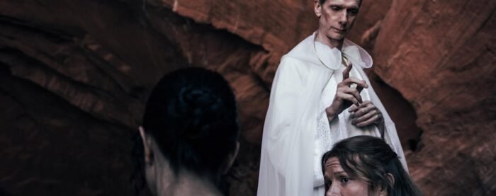 A priestly man stands over a couple of people appearing to bless them