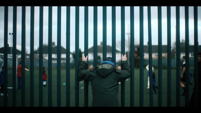 A man watching a children's soccer game through the bars of a gate.