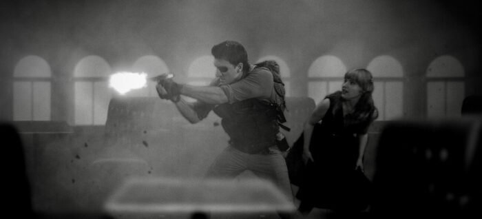 A woman ducks behind a man firing his gun on a foggy ship.