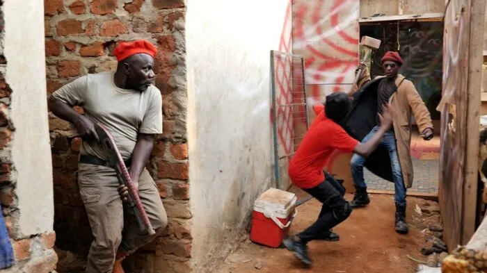 A man with a gun takes cover behind a corner while another man appears to be raising a weapon against a fleeing individual.