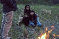 A woman consoles a younger woman in a field inches from a fire