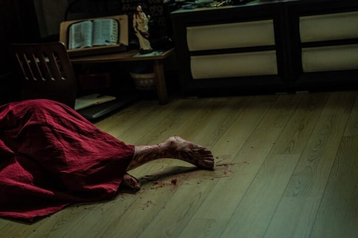 A woman drags her bloody foot across a wooden floor.