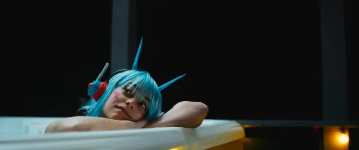 A woman with blue hair wearing a toy headset giving her demon horns, leans against the inside of a bathtub (Appofeniacs / FrightFest)