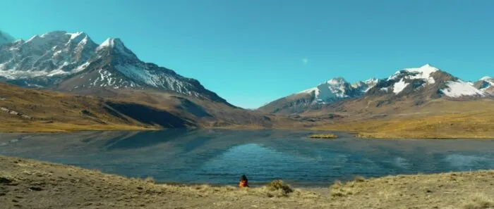 A young girl crouches in front of a lake vista.