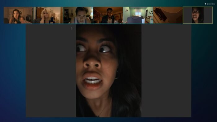 a spotlit Zoom chat with many video streams sitting above a zoomed in vertical face in the dark.