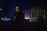 A woman sings on stage in front of a blue curtain and giant speakeasy sign (Every Heavy Thing)