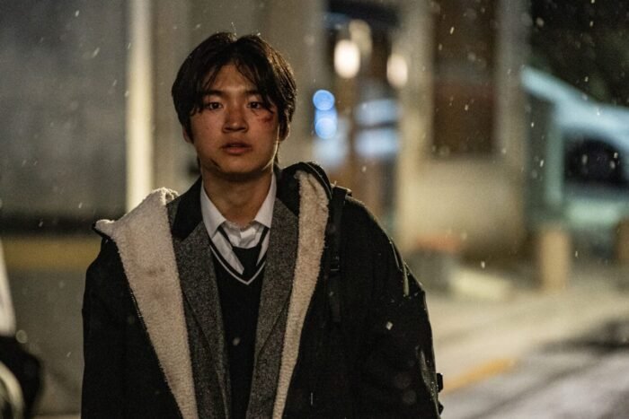 A young man in a winter coat standing beside a building on the street.