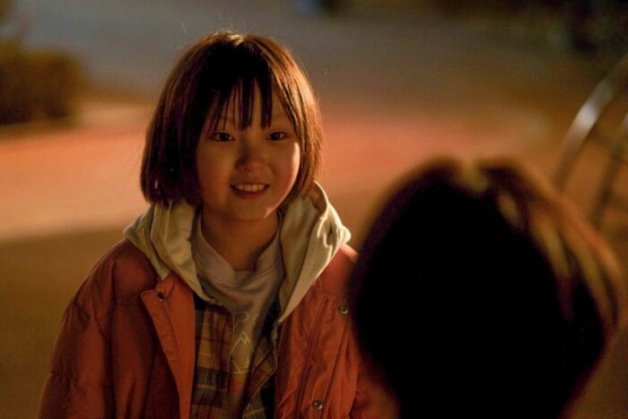 A young girl smiles at an out of focus person in the foreground (Fragment)