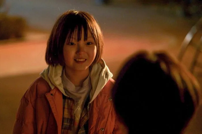 A young girl smiles at an out of focus person in the foreground (Fragment)