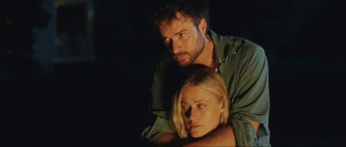 A man wraps his arms around a woman's neck from behind her.