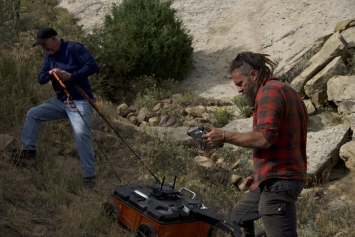 Chad Ollinger and James Keenan haul a heavy GPR device across the ranch's steep terrain as they search for underground caverns.