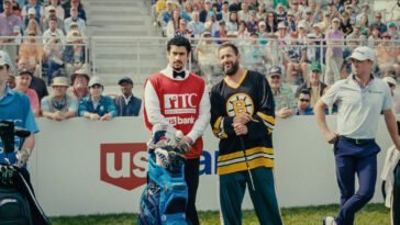 Happy Gilmore and his caddy talk while fans surrounding them look on.