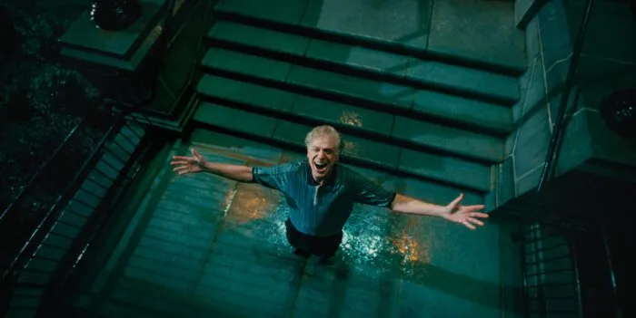 A man outstretches his arms in the rain at the bottom of a cement staircase.