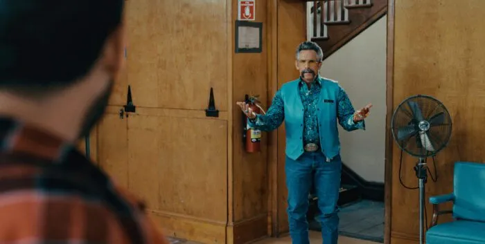 A man dressed in all blue holds his hands up in surprise as he enters a room (Happy Gilmore 2)