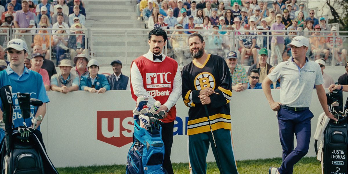 Happy Gilmore and his caddy talk while fans surrounding them look on.