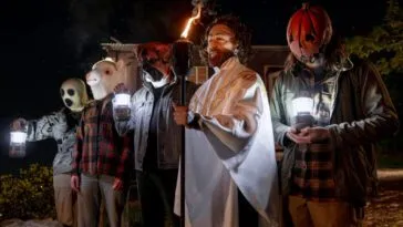 a group of masked individuals stand in a line, one is holding a torch (Self-Help)