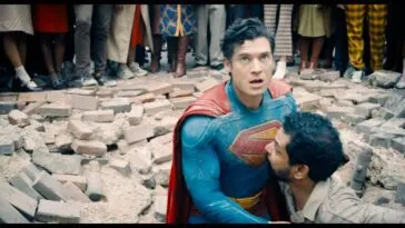 A man helps Superman out of a huge hole of rubble concrete