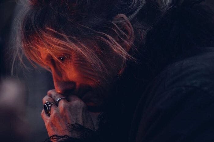 A woman holding her closed hands to her face is lit by a fire.