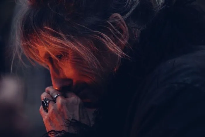 A woman holding her closed hands to her face is lit by a fire.