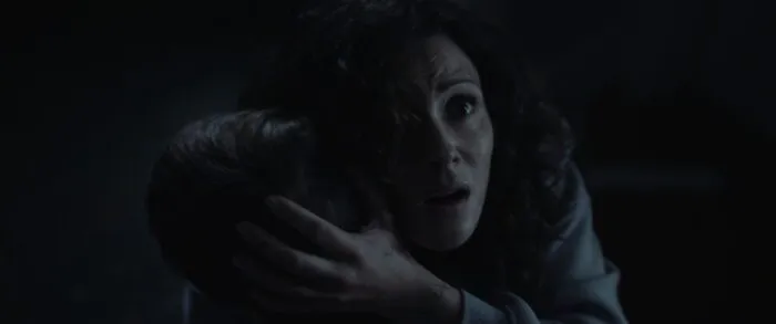 A woman holds her son in her arms while looking up toward the camera in horror (The Confession)