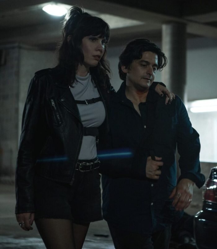 A tall woman with her arm around a shorter man, walking through a parking garage together.