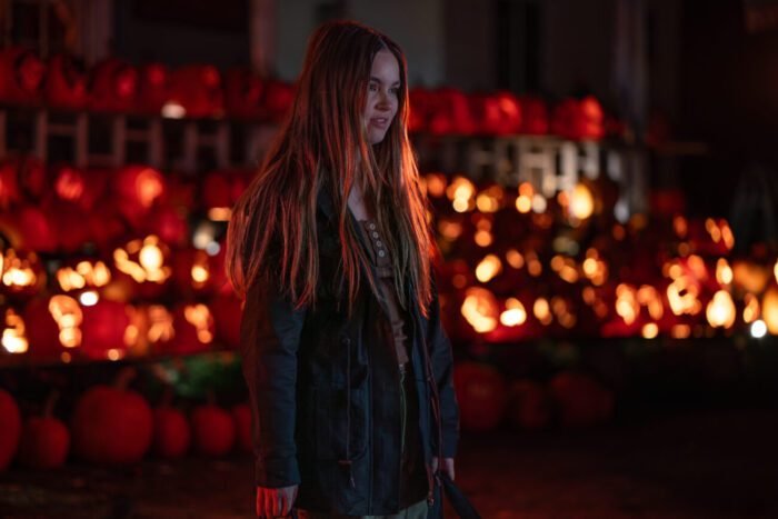 A woman stands in front of an array of flame-lit pumpkins on a porch (Self-Help)