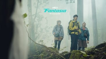 something in the foreground catches the attention of three individuals standing on a high rock in the fog of a forest.