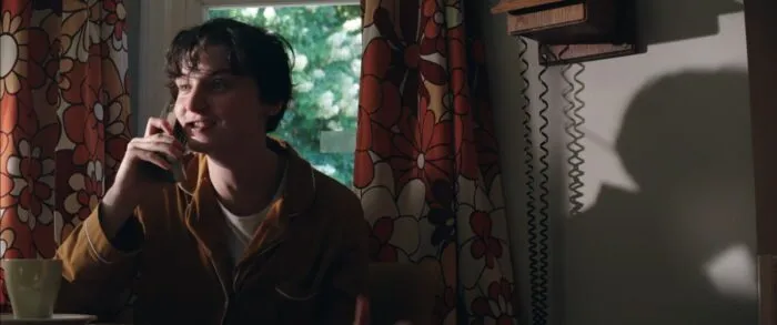 Tessa speaks on an analog phone while the loud, flowery curtains dangle in the background and Tessa's shadow fills the wall space to their left. 