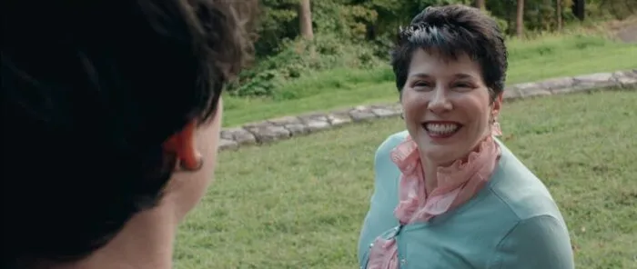 A woman gives a toothy grin to the person standing in the doorway.